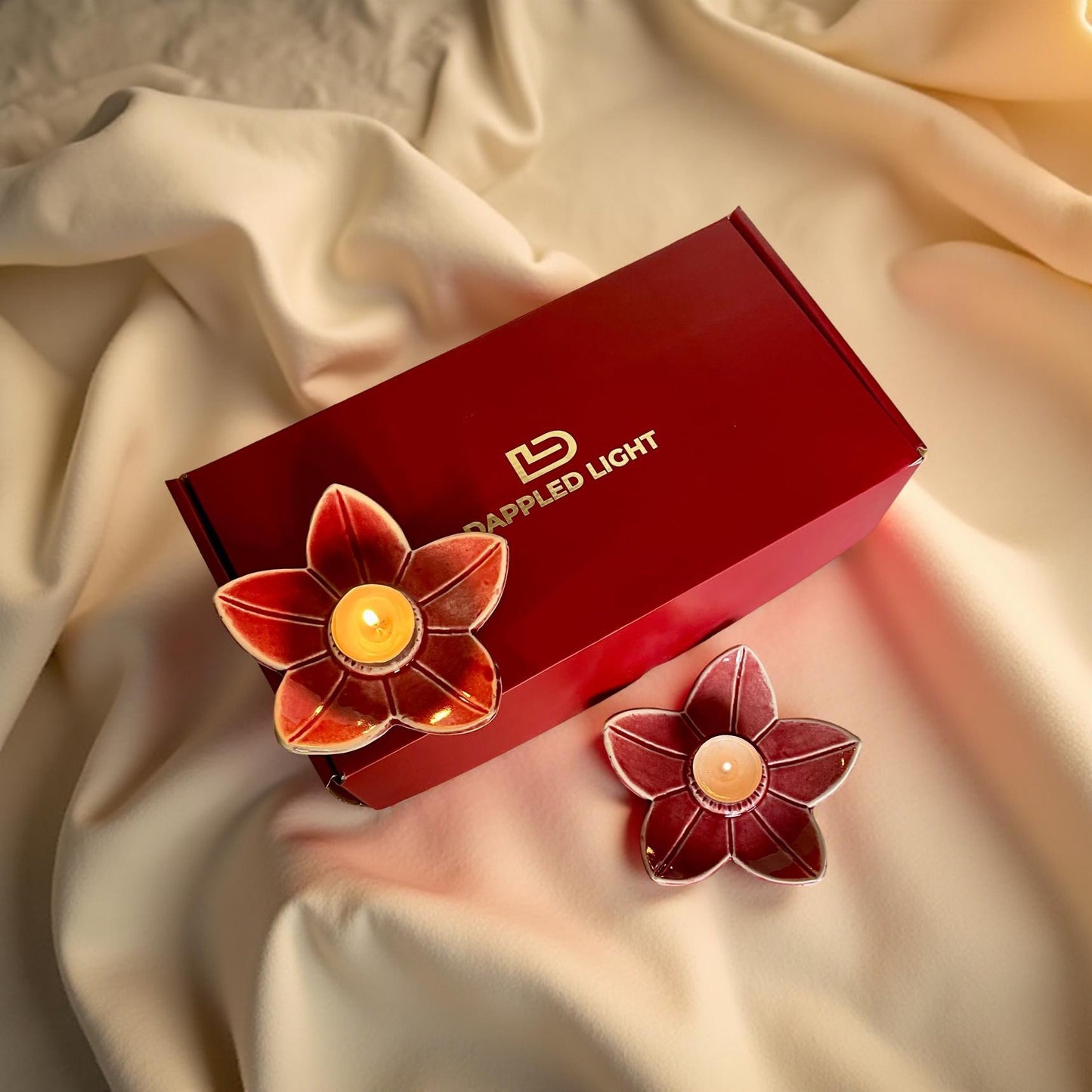 A set of two deep pink ceramic lotus-shaped tea light holders, presented next to their red gift box with the brand 'Illuminated Light' visible on it.