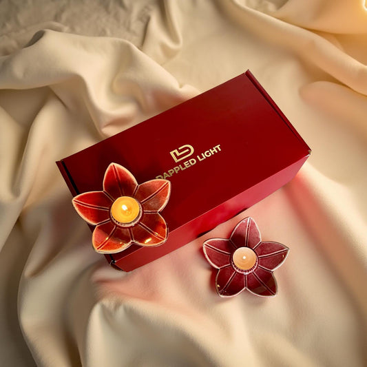A set of two deep pink ceramic lotus-shaped tea light holders, presented next to their red gift box with the brand 'Illuminated Light' visible on it.